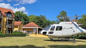 A white helicopter with "HEILAUSANNE" on its side parked in front of a yellow building with a red roof.