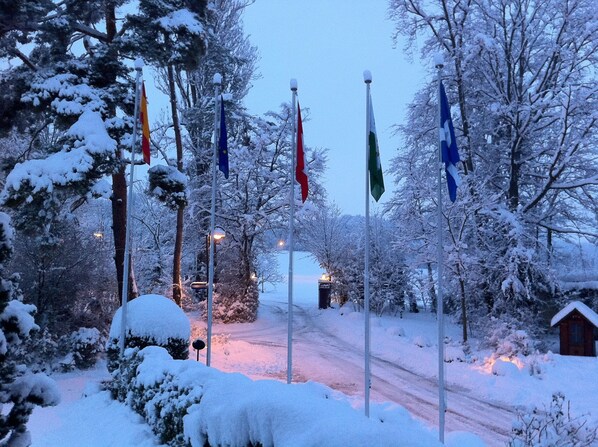 A snowy landscape with multiple flags on poles, a snow-covered path, and a small building in the background. - Hotel La Barcarolle (Prangins)