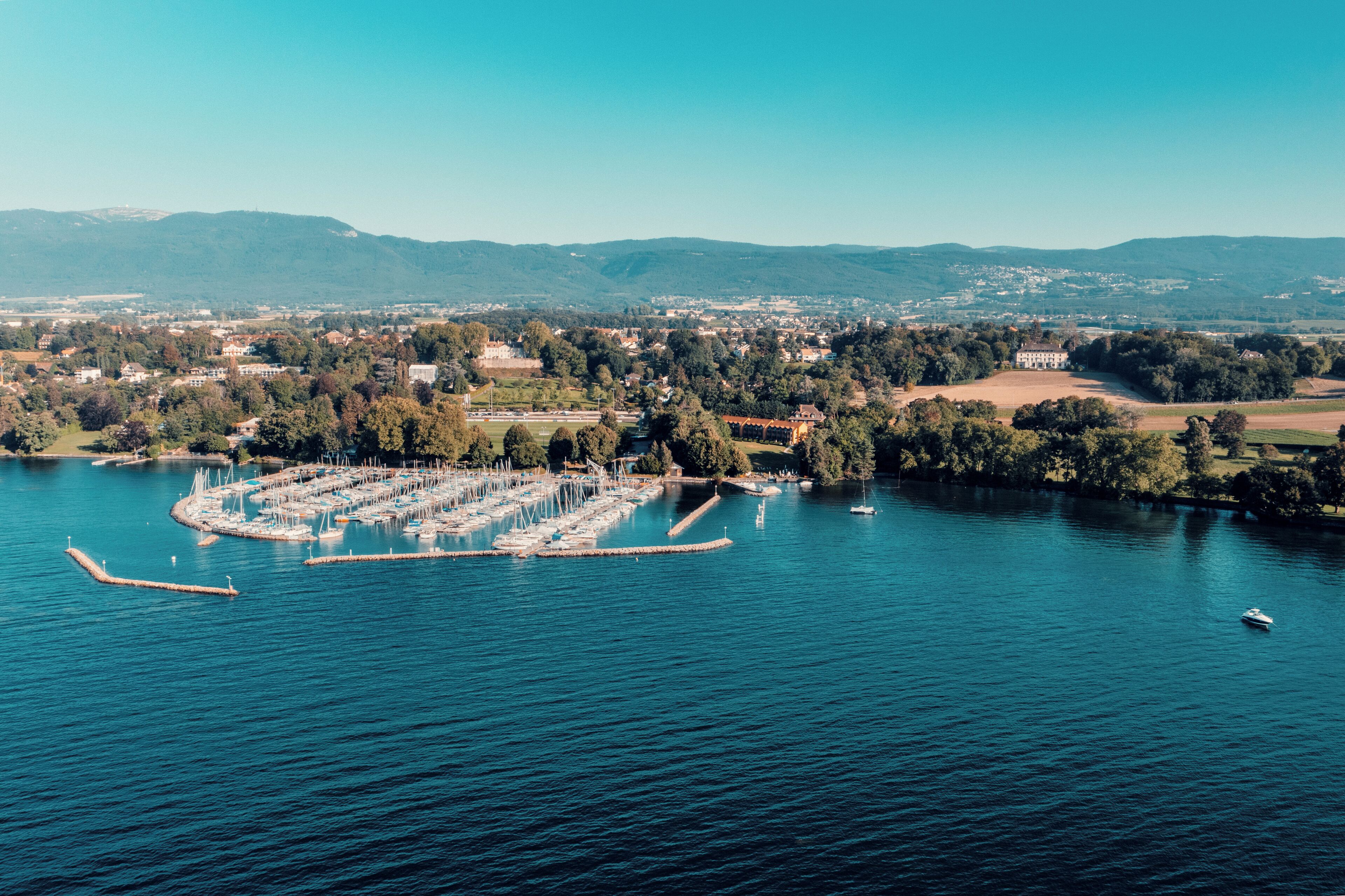 An aerial view of a marina with boats docked, surrounded by hills and a town in the distance.
