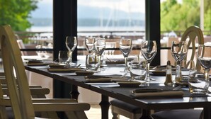 A dining table set for a meal with a view of the sea and a bridge in the background. - Hotel La Barcarolle (Prangins)