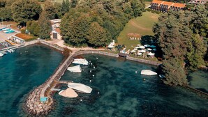 An aerial view of a waterfront property with a dock, boats, and a small building. - Hotel La Barcarolle (Prangins)