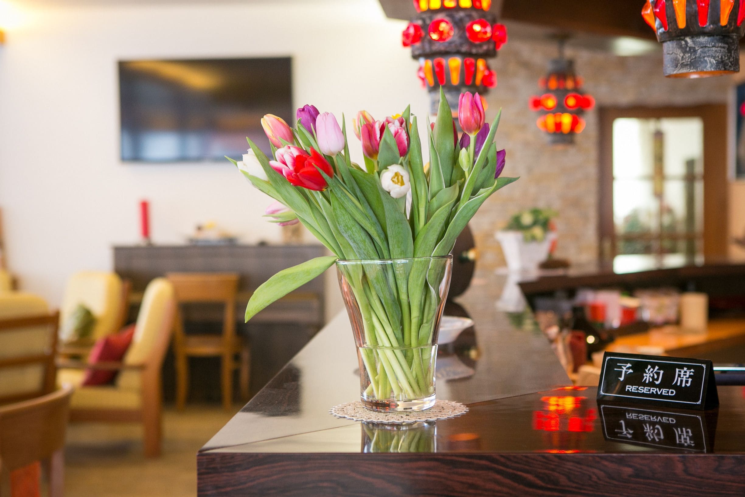 A glass vase with tulips on a wooden counter in a hotel lobby.