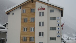 A hotel with a wooden facade and multiple windows, surrounded by snow. - Hotel Mountime (Taesch)