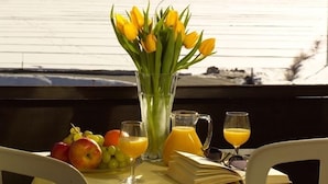 A dining table with a bouquet of yellow tulips, a fruit plate, and two glasses of orange juice, set against a mountain view. - Hotel Mountime (Taesch)