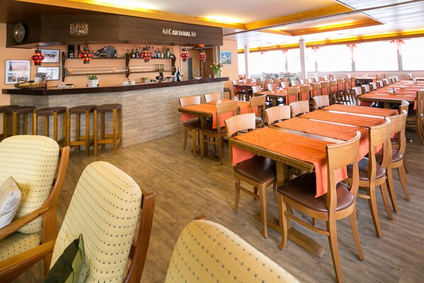 A restaurant with multiple tables and chairs, a bar area with various bottles and a sign reading "CARDINAL". - Hotel Mountime (Taesch)