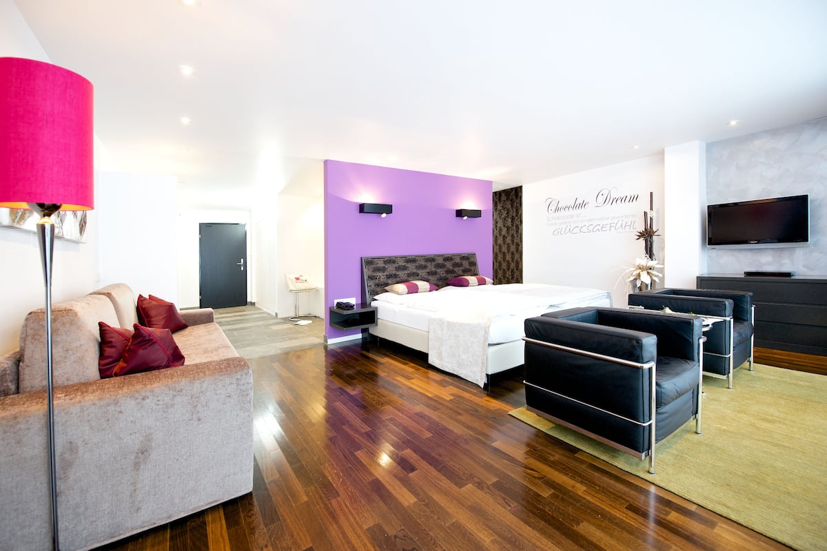 A modern bedroom with a bed, a sofa, a TV, and a wall with a sign.