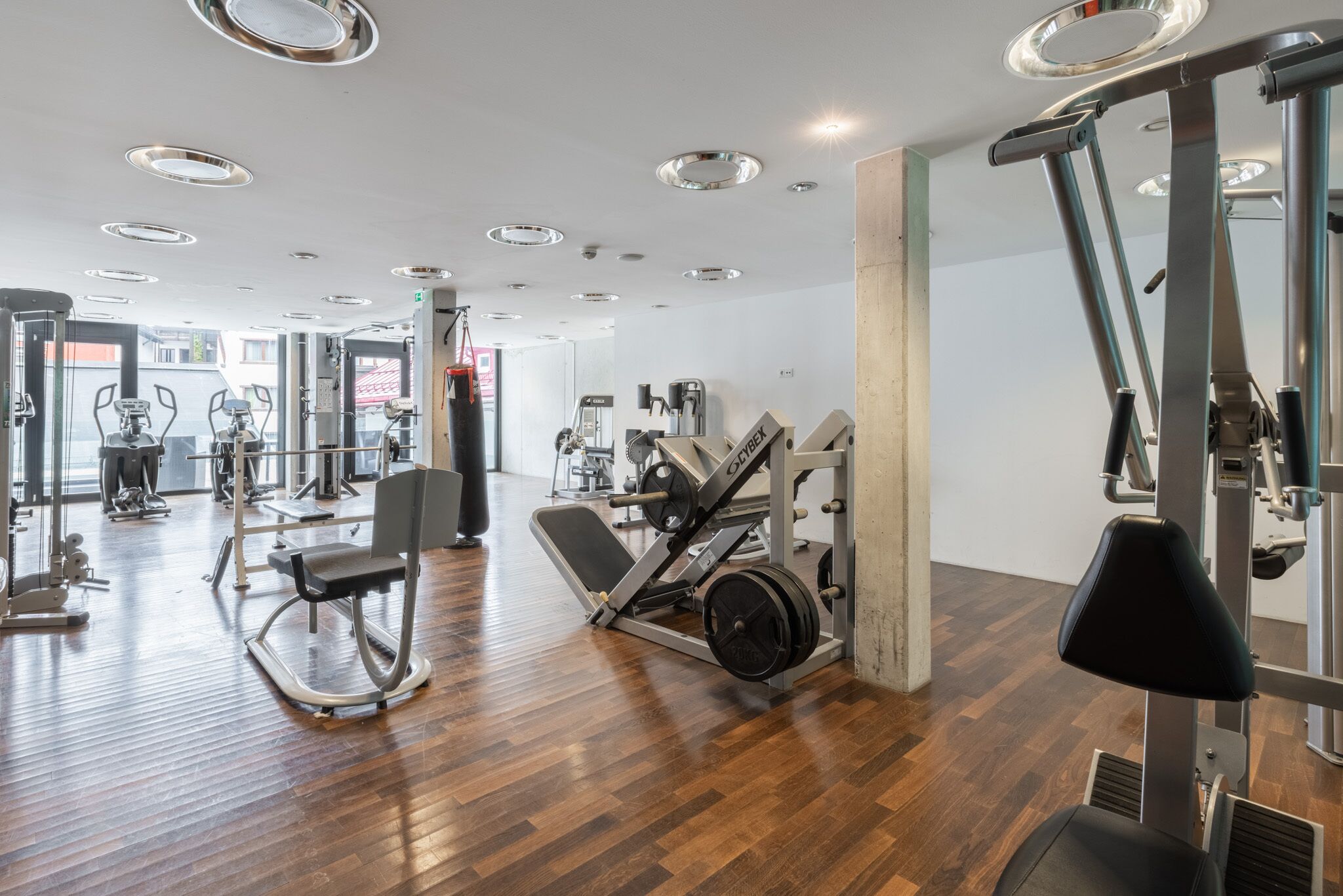 A modern gym with various exercise equipment, wooden flooring, and a bright, well-lit interior.