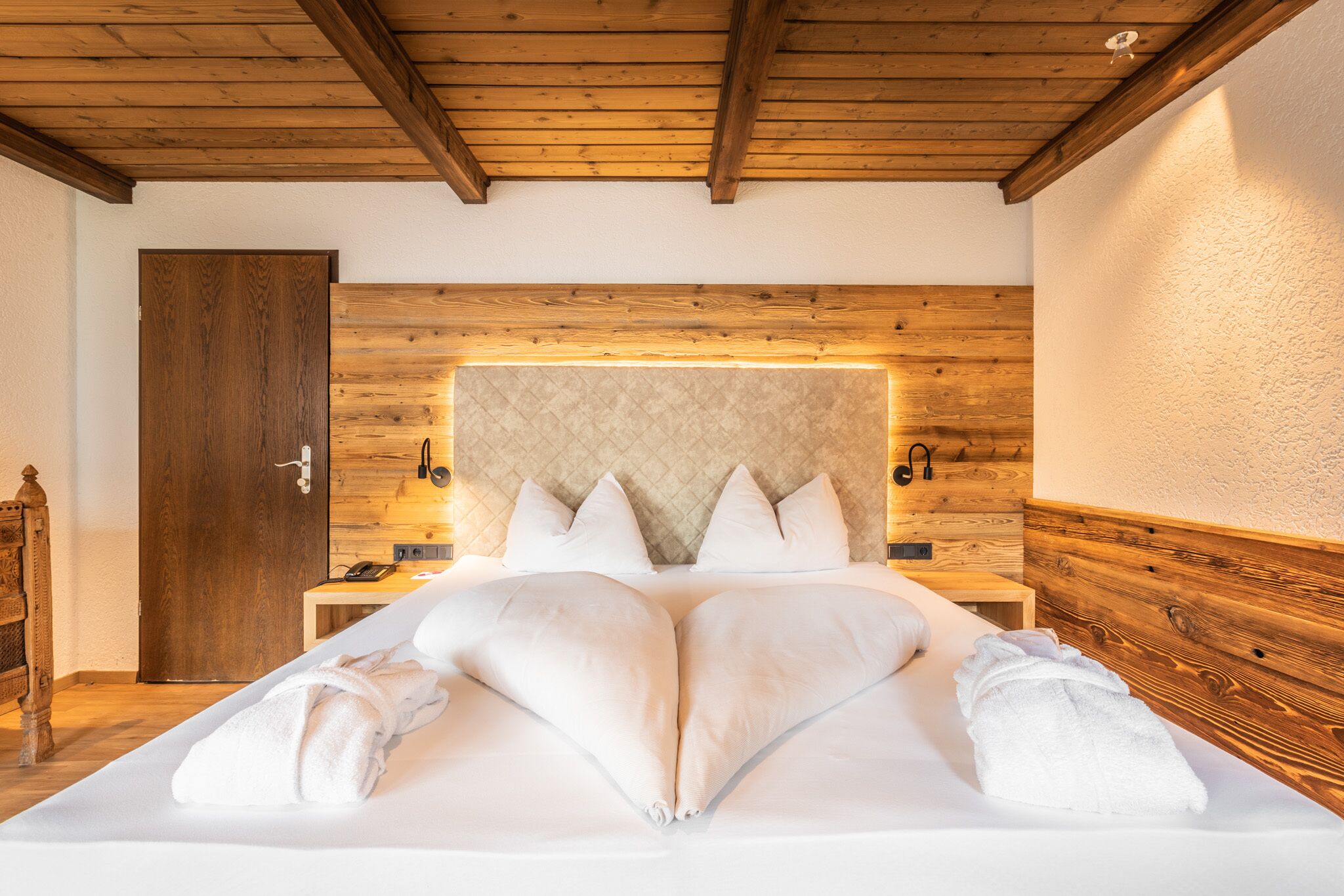 A bedroom with a wooden ceiling, a large bed with white linens, and a headboard with a quilted design.