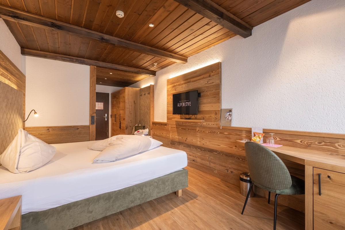 A room with a bed, a desk, and a television on the wall.