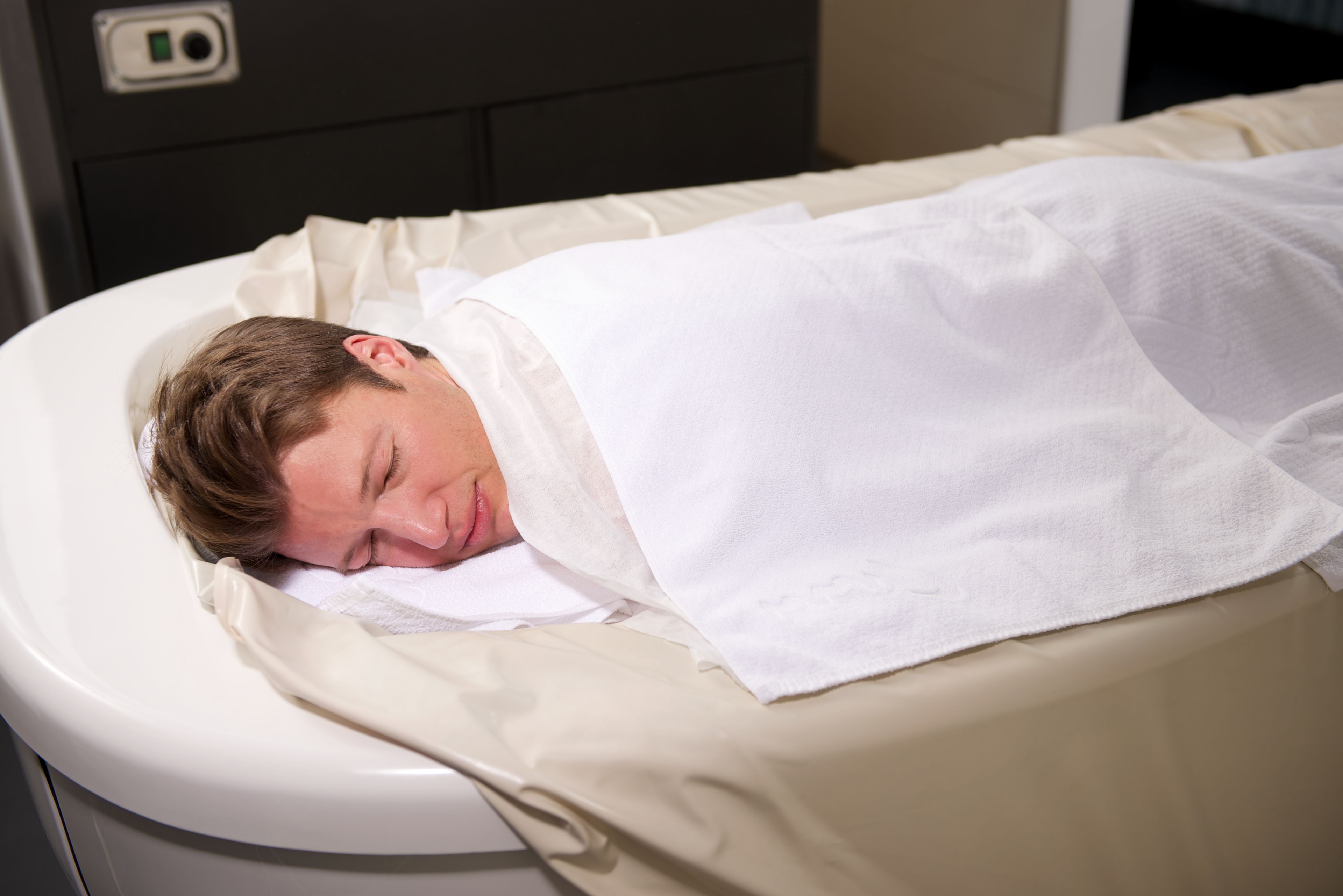 Una persona acostada en una cama con una manta blanca.