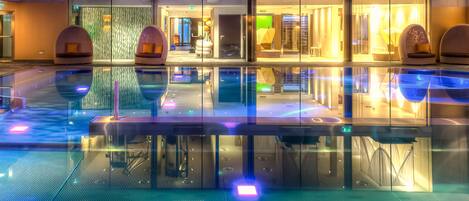 Un moderno vestíbulo de hotel con una amplia piscina interior, puertas de vidrio y zonas de estar.