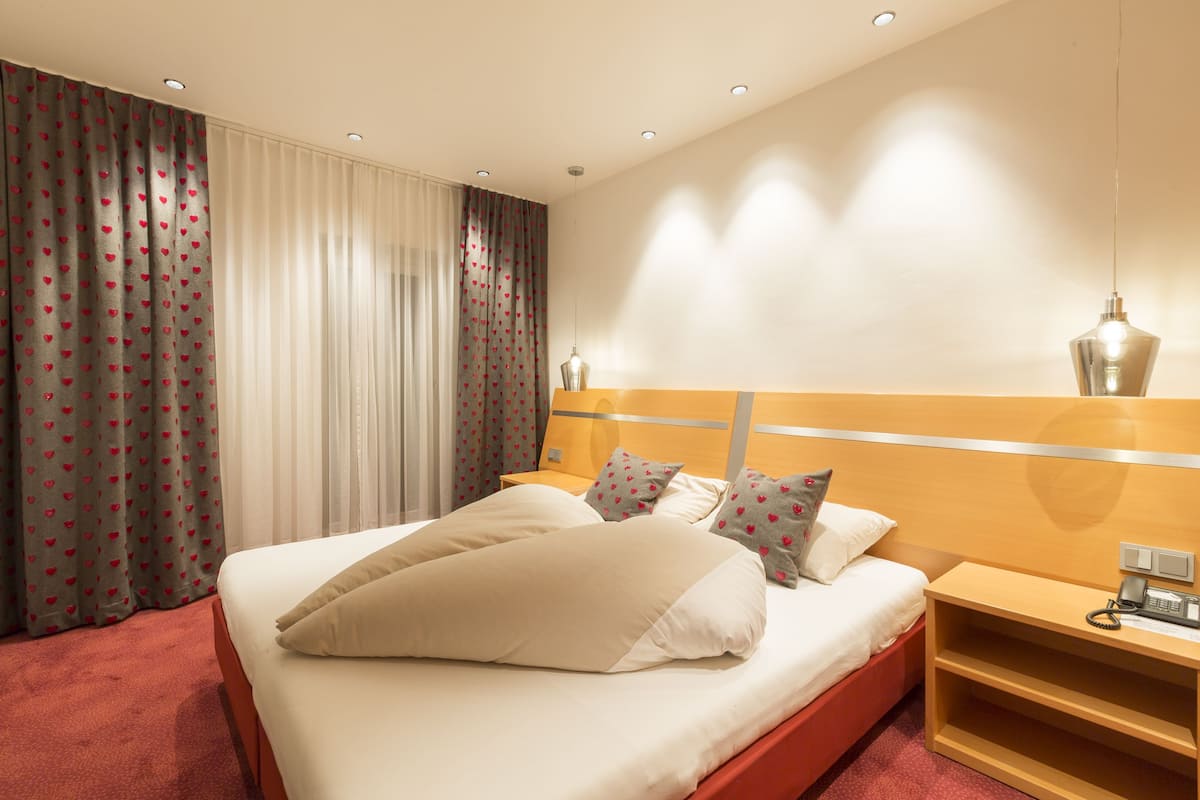 A hotel room with a large bed, a wooden nightstand, a telephone, and a lamp.