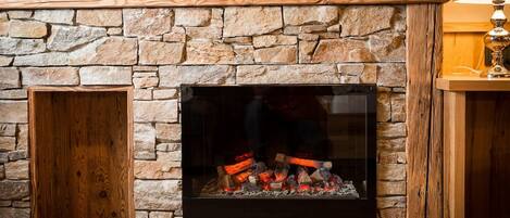 A stone fireplace with a wooden mantel, a glass door, and a visible fire.