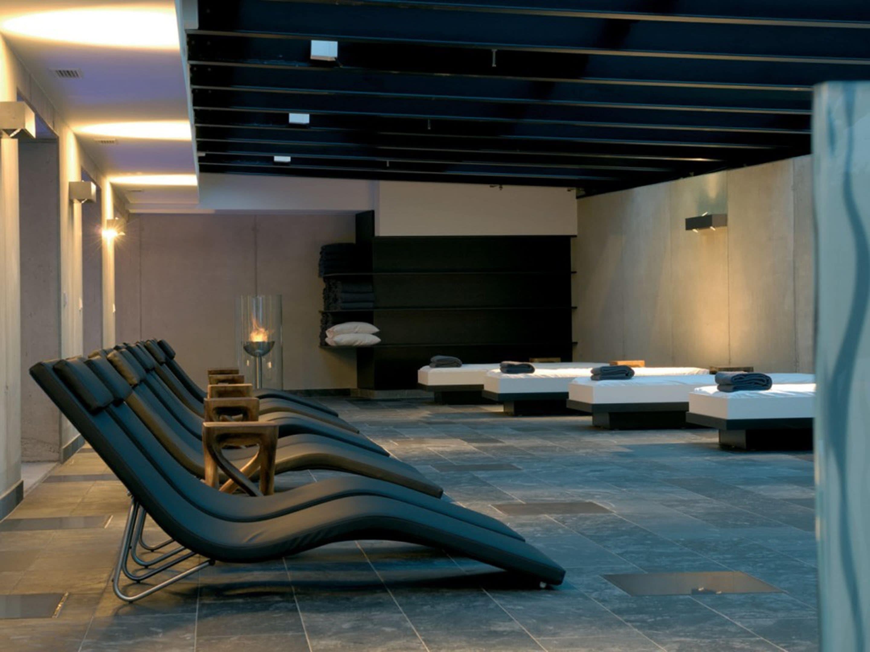Ein moderner Wellnessraum mit Massageanlayte, einem kleinen Kamin und mehreren Massageliegen.