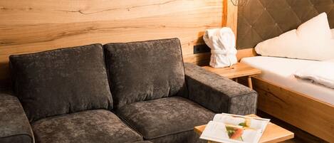 A modern room with a dark grey sofa, a wooden wall, a bed with white bedding, and a small table with a magazine.