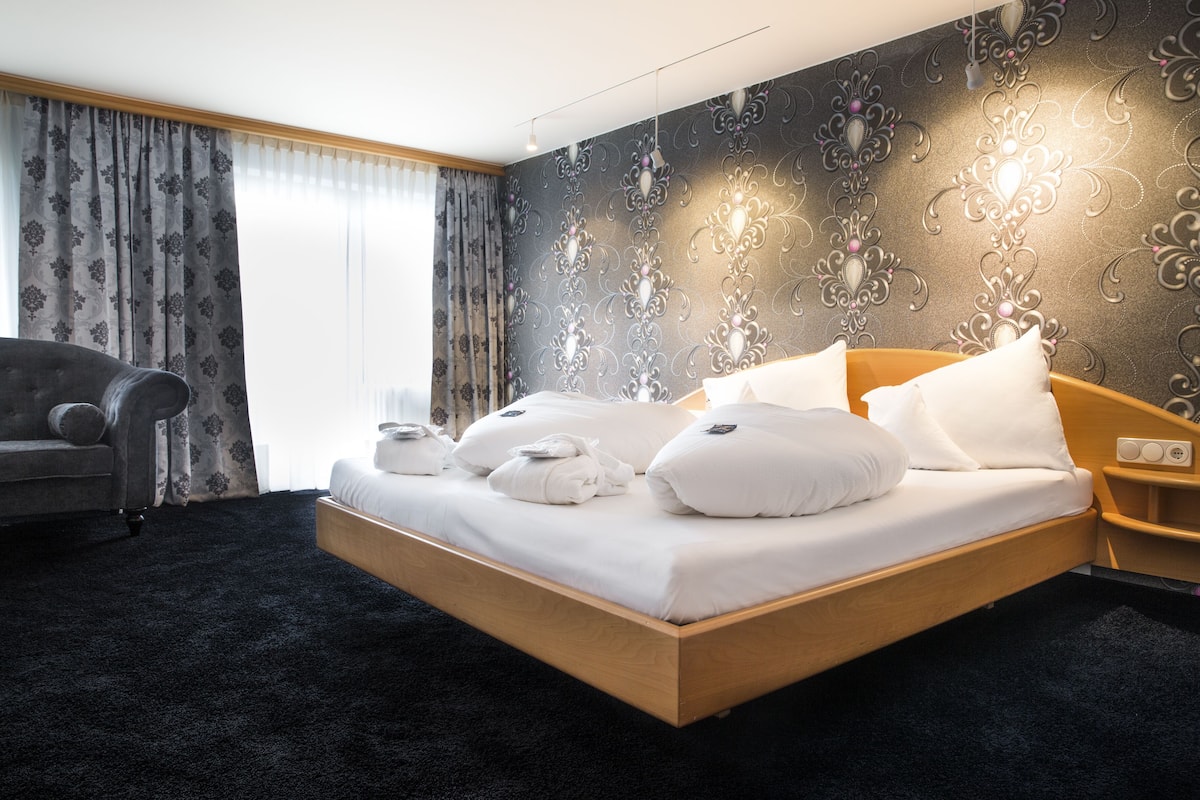 A hotel room with a large bed, a bedside table, a chair, and a wall with a decorative pattern.