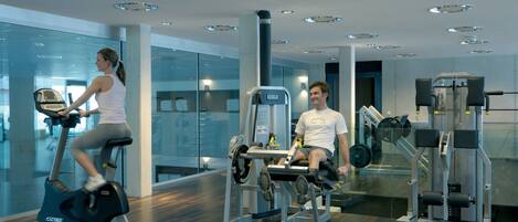 Ein modernes Fitnessstudio mit Cardiogeräten, Krafttrainingsgeräten und einer Glaswand mit Blick ins Innere.