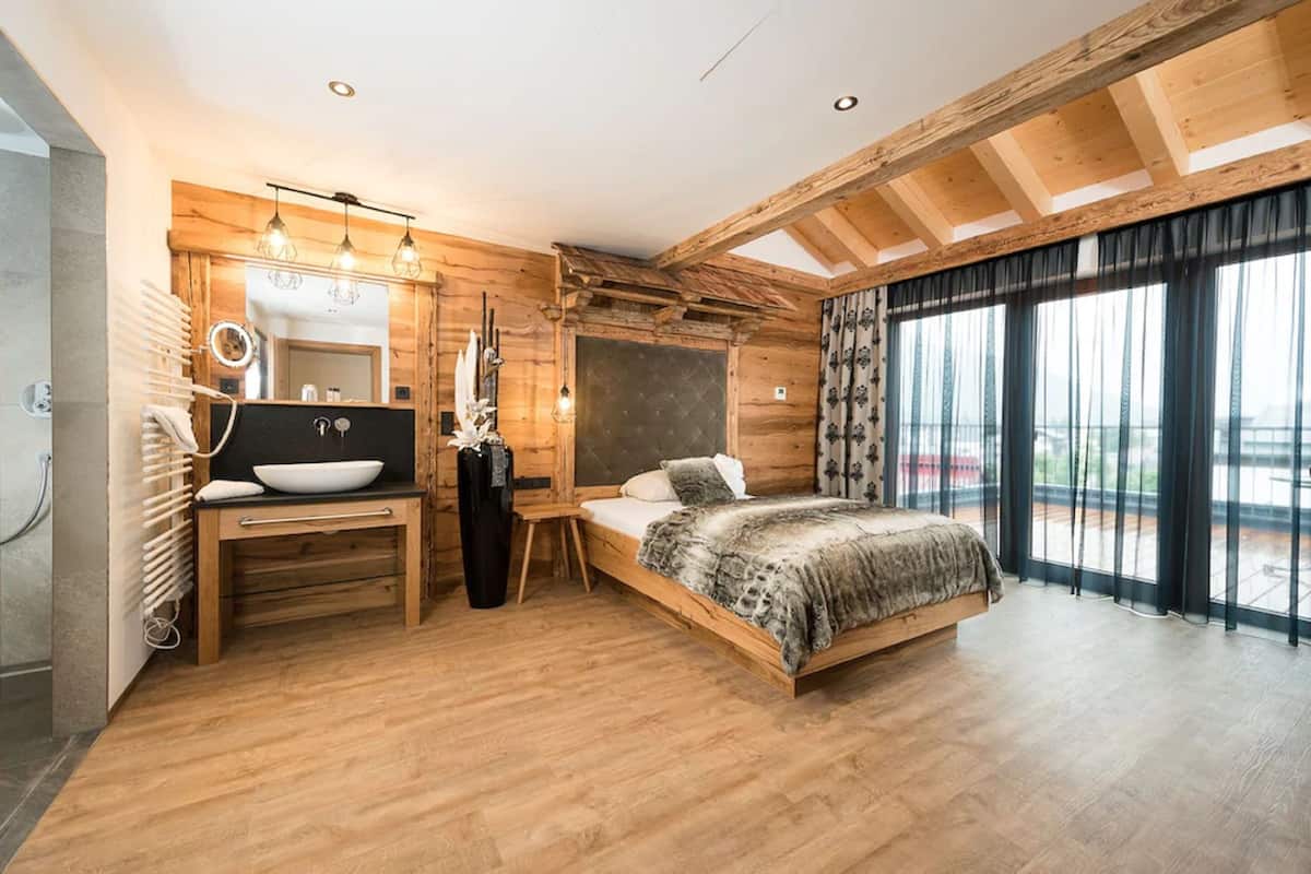 A wooden cabin-style bedroom with a large bed, a wooden desk with a bowl, and a view of the outdoors through large windows.