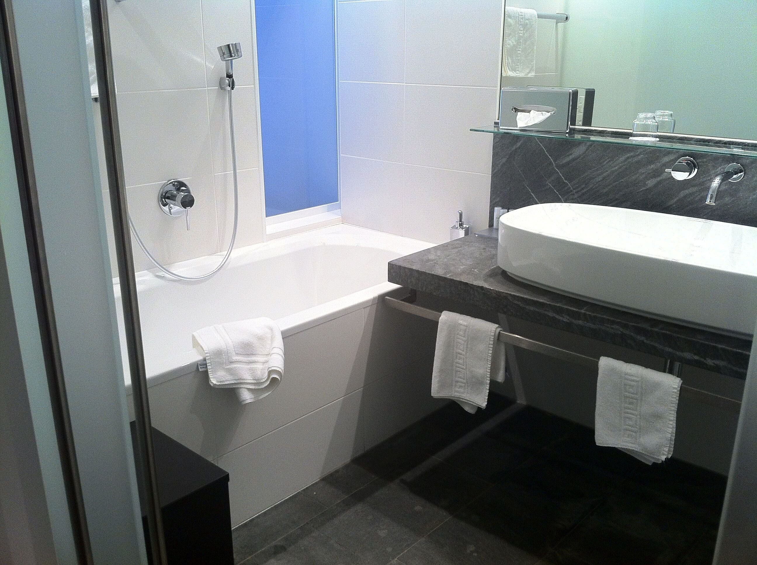 A modern bathroom with a bathtub, a glass-enclosed shower, and a marble countertop with a sink.
