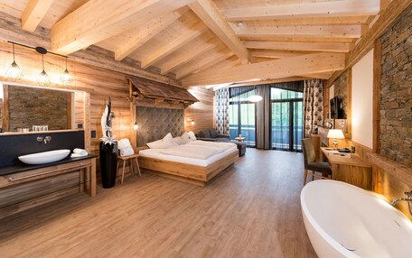 A wooden cabin interior with a large bed, a bathroom with a bathtub, and a stone wall.