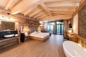 A wooden cabin interior with a large bed, a bathroom with a bathtub, and a stone wall. - Alpenlove - Adult SPA Hotel (Seefeld in Tirol)