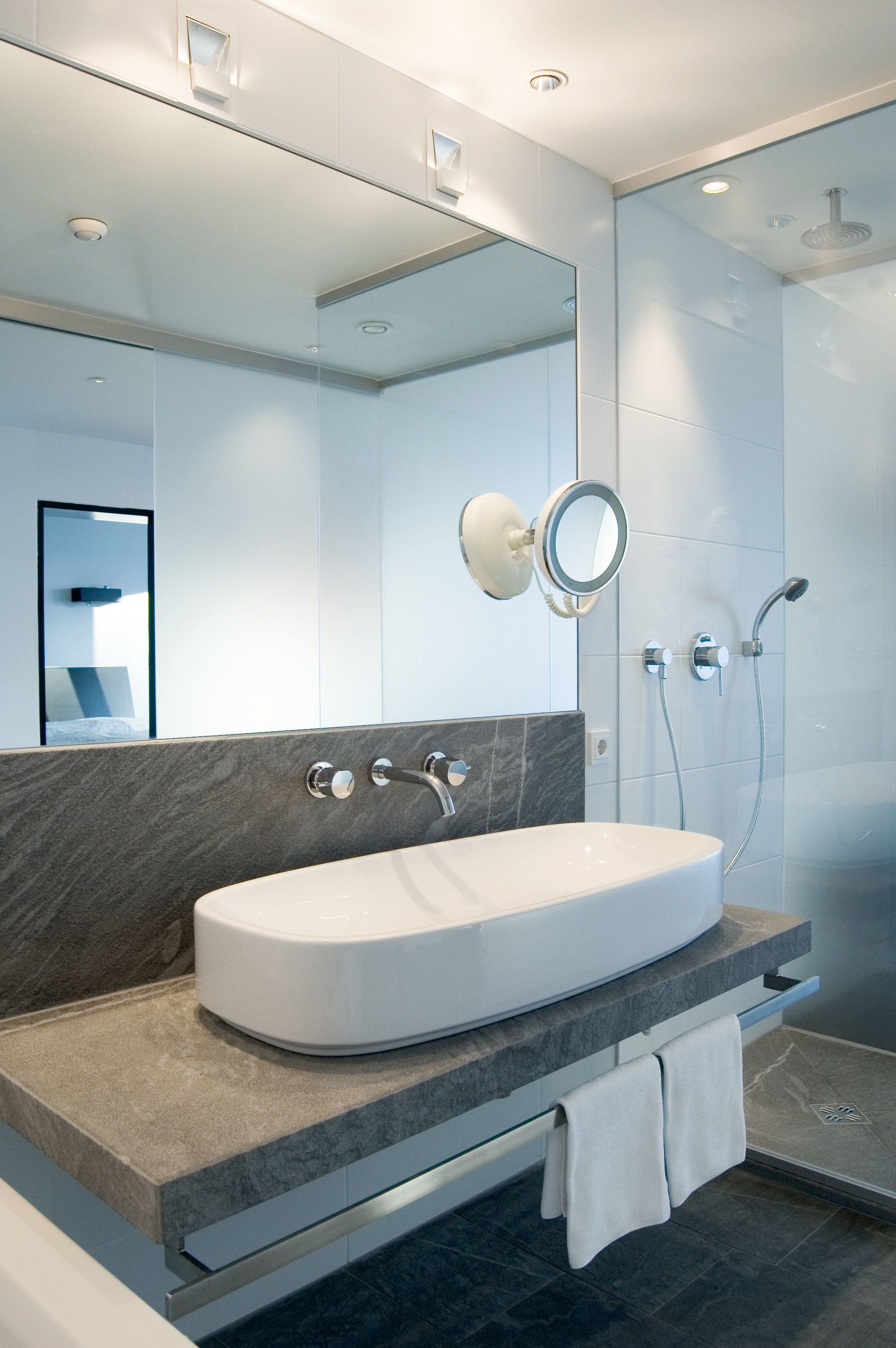 A modern bathroom with a large oval sink, a mirror, and a shower.