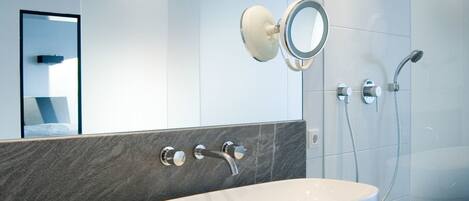 A modern bathroom with a large oval sink, a mirror, and a shower.