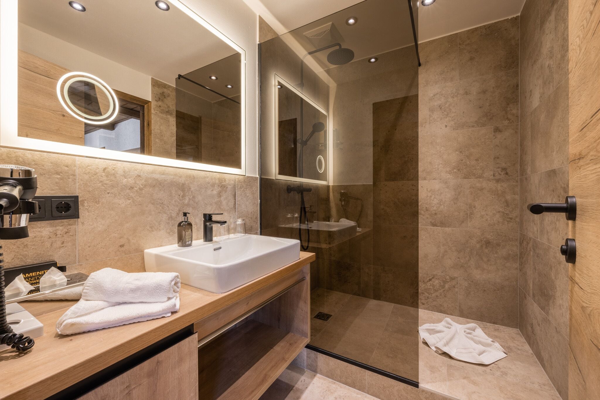 Un bagno moderno con un ampio specchio, un lavandino bianco e una cabina doccia in vetro.