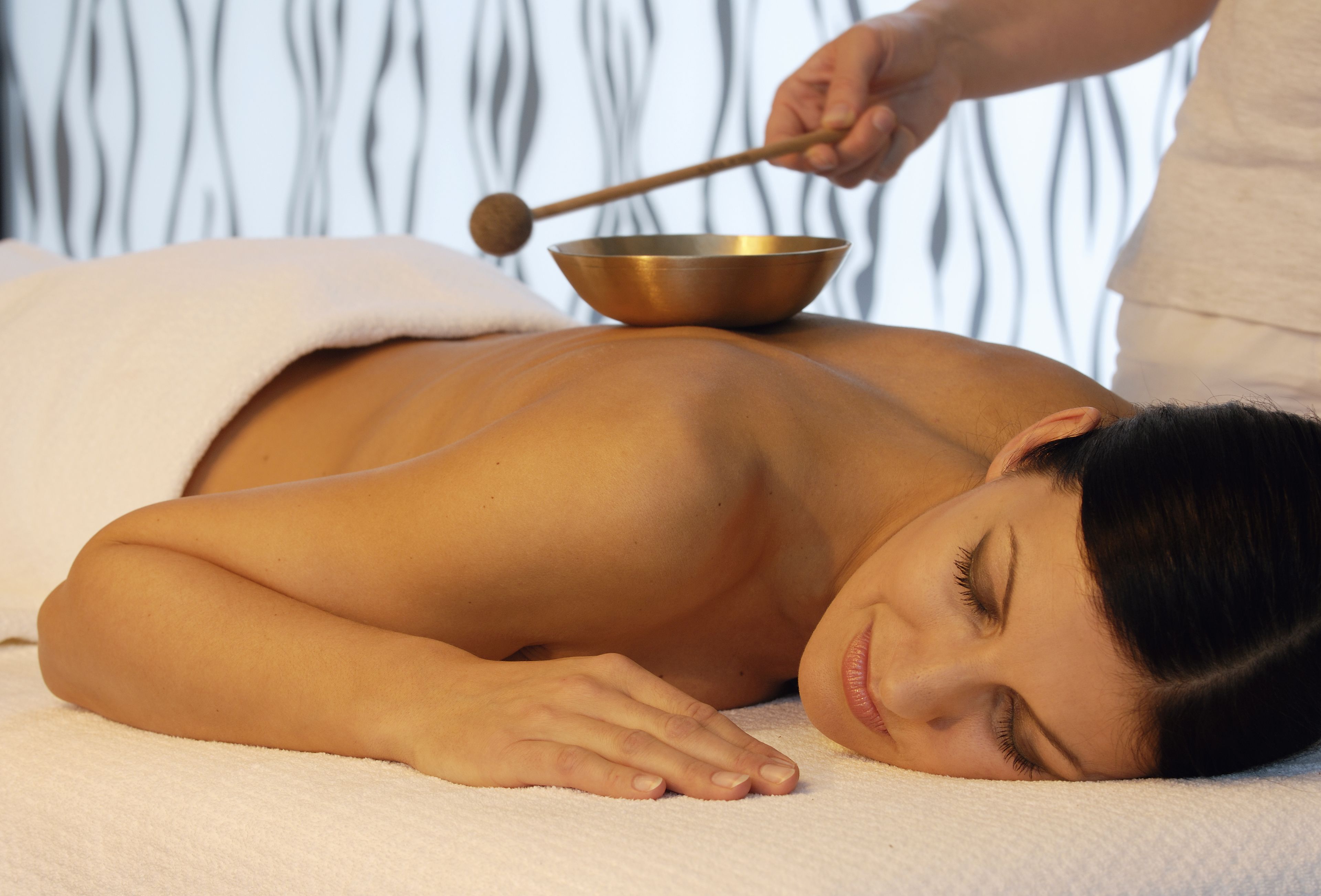 A person receiving a massage with a wooden mallet and a metal bowl.