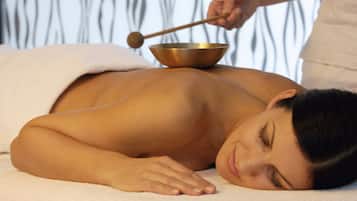 A person receiving a massage with a wooden mallet and a metal bowl.