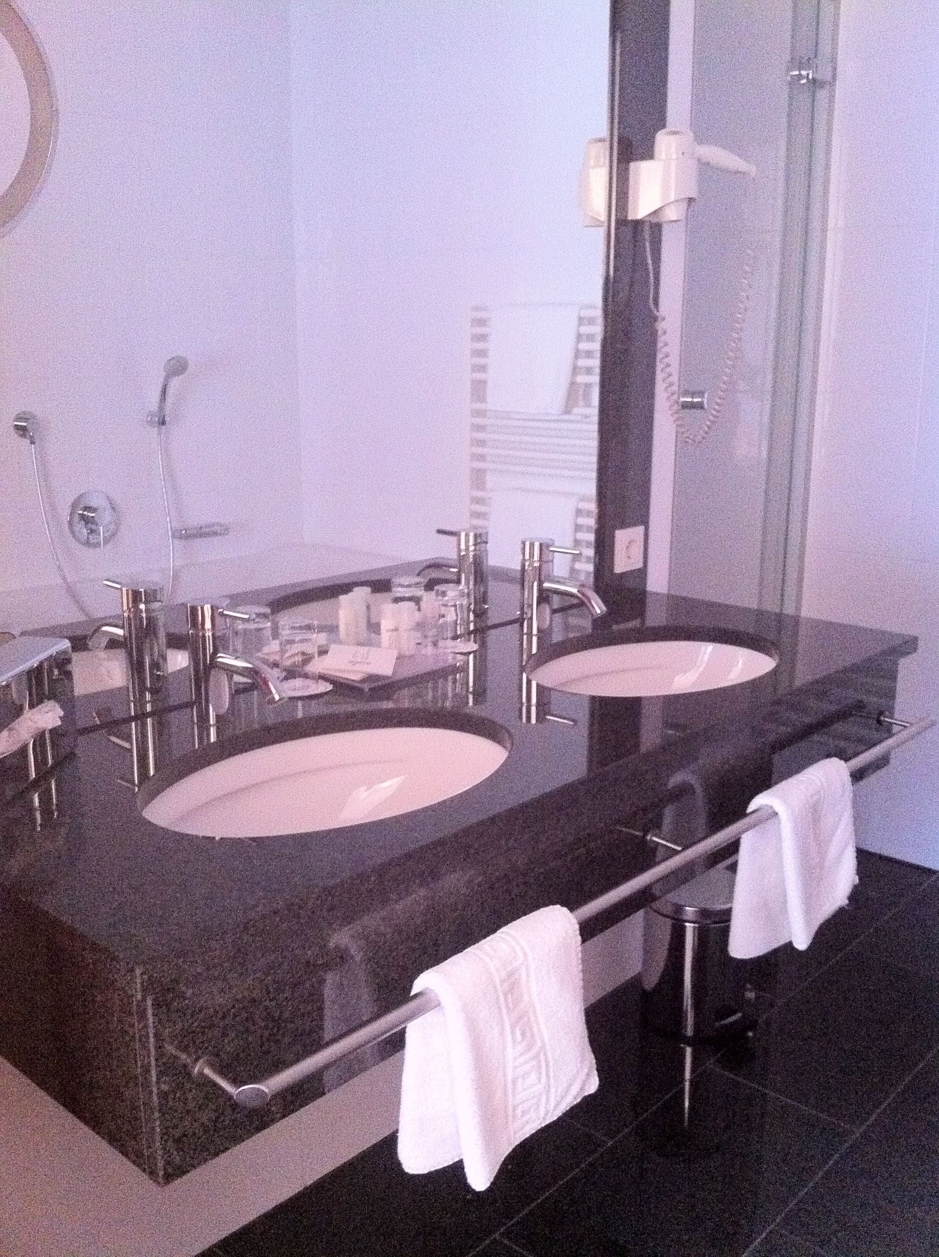 Un baño moderno con dos lavamanos, cabina de ducha de vidrio y un perchero para toallas.