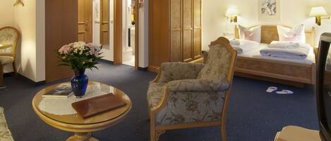 A hotel room with a bed, a chair, a table with a vase, and a wardrobe.