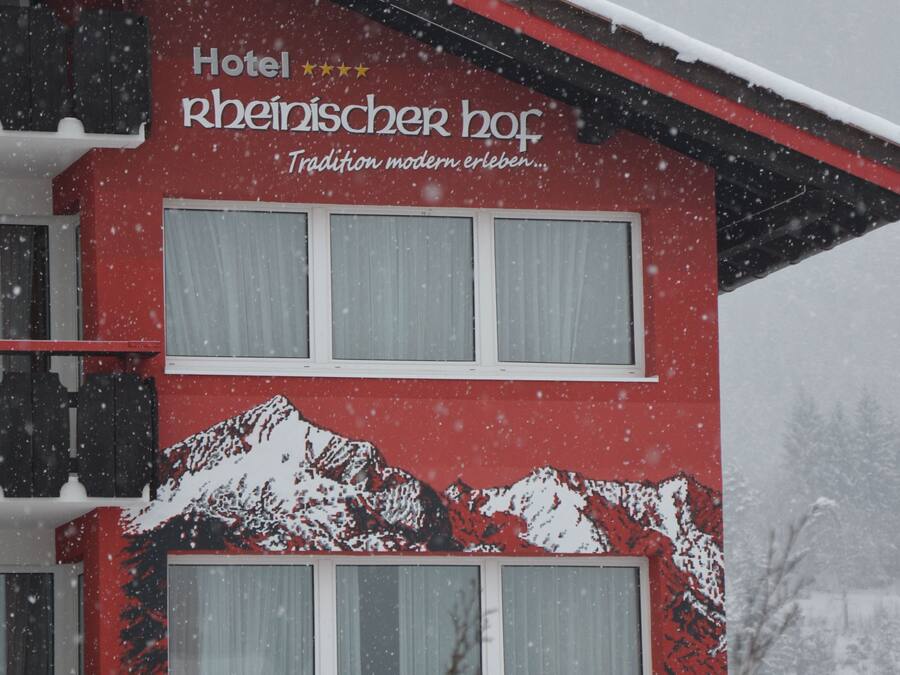 A red building with the sign "Hotel Rheinischer Hof" and a mountain design.