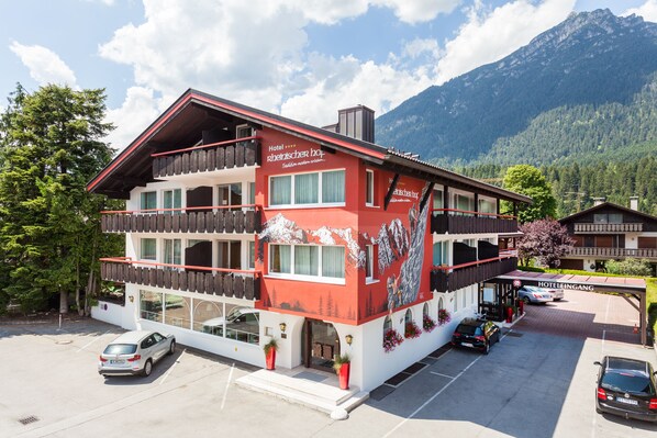 A hotel with a red facade, balconies, and a mountain backdrop.