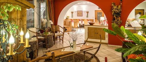 A rustic interior with wooden beams, a dining area, and a kitchen visible through an archway.