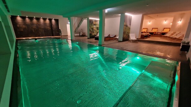 An indoor swimming pool with green lighting, lounge chairs, and a staircase. - Hotel Rheinischer Hof (Garmisch-Partenkirchen)
