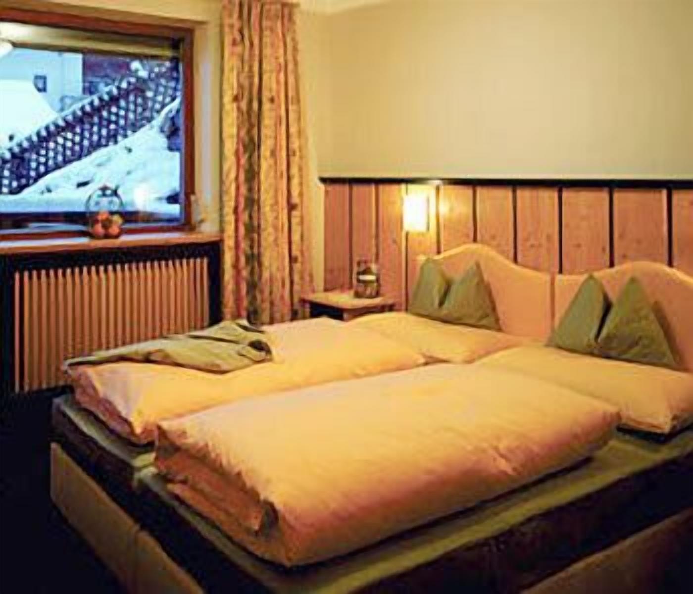 A double bed with two pillows, a nightstand with a lamp, and a window with curtains.