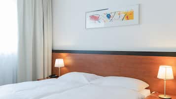 A hotel room with a bed, two bedside lamps, a wooden headboard, a framed abstract painting, and a window with curtains.