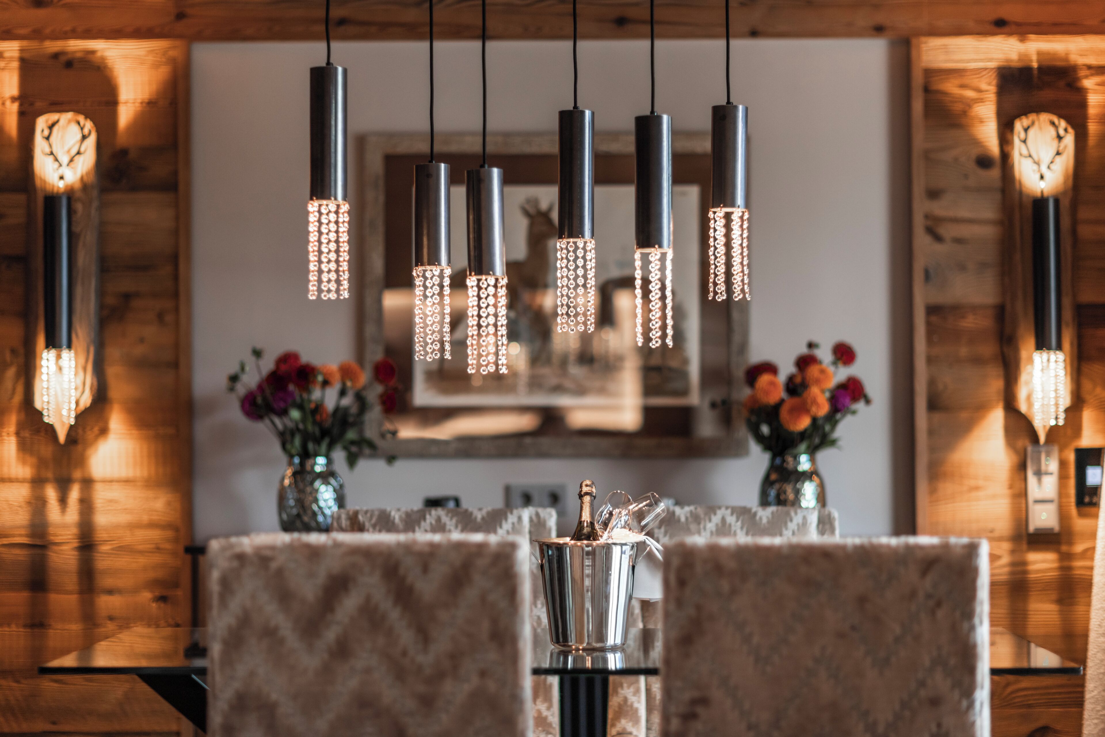 A dining area with a wooden wall, pendant lights, a table with a vase of flowers, and a clock on the wall.