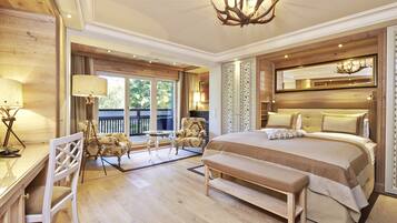 A spacious bedroom with a large bed, a desk, and a chair. There is a balcony with a view of greenery.