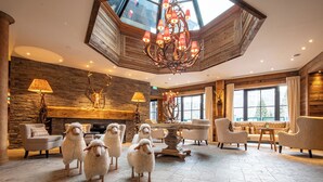 A spacious lobby with a stone fireplace, a chandelier, and a large window. - Alpin Resort Sacher (Seefeld in Tirol)
