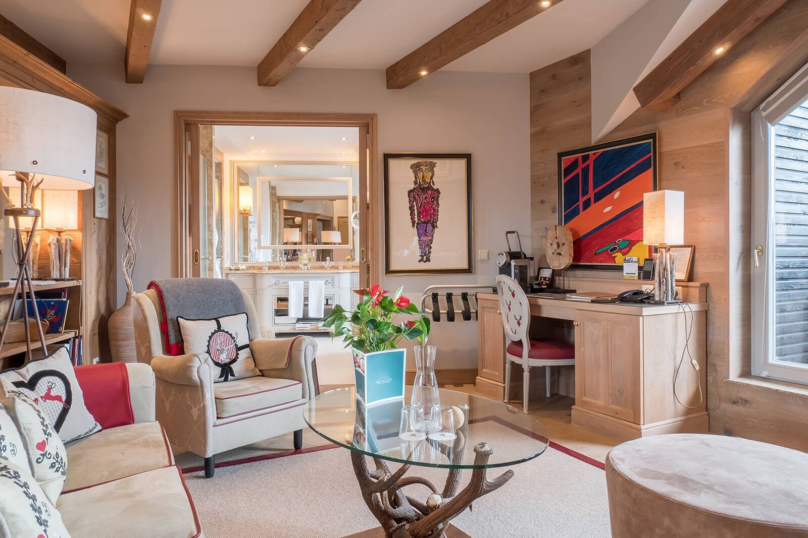 A spacious living room with a glass coffee table, a sofa, and a dining area with a wooden desk and chair.