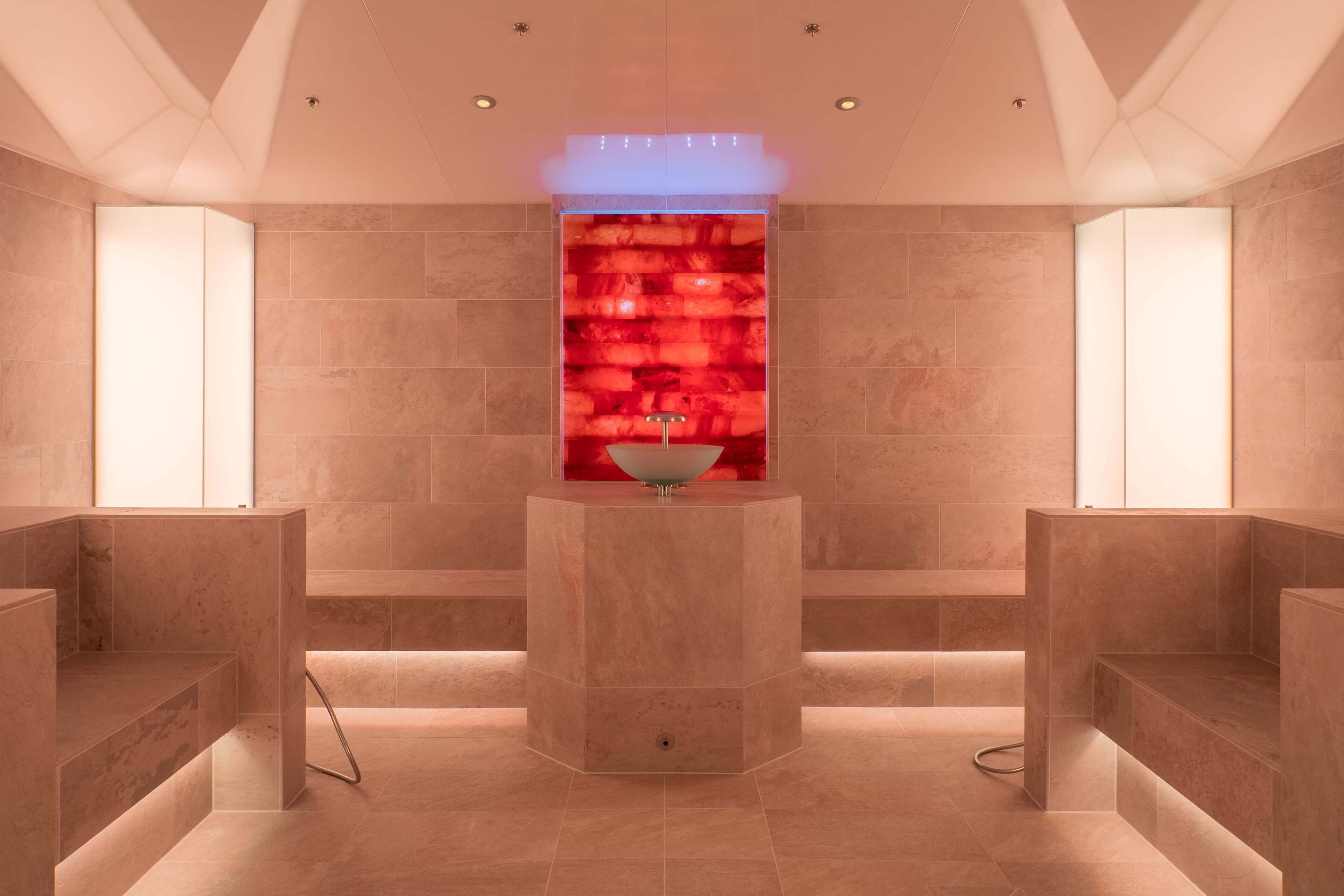 A modern spa room with a central heated stone wall, recessed lighting, and a minimalist design.