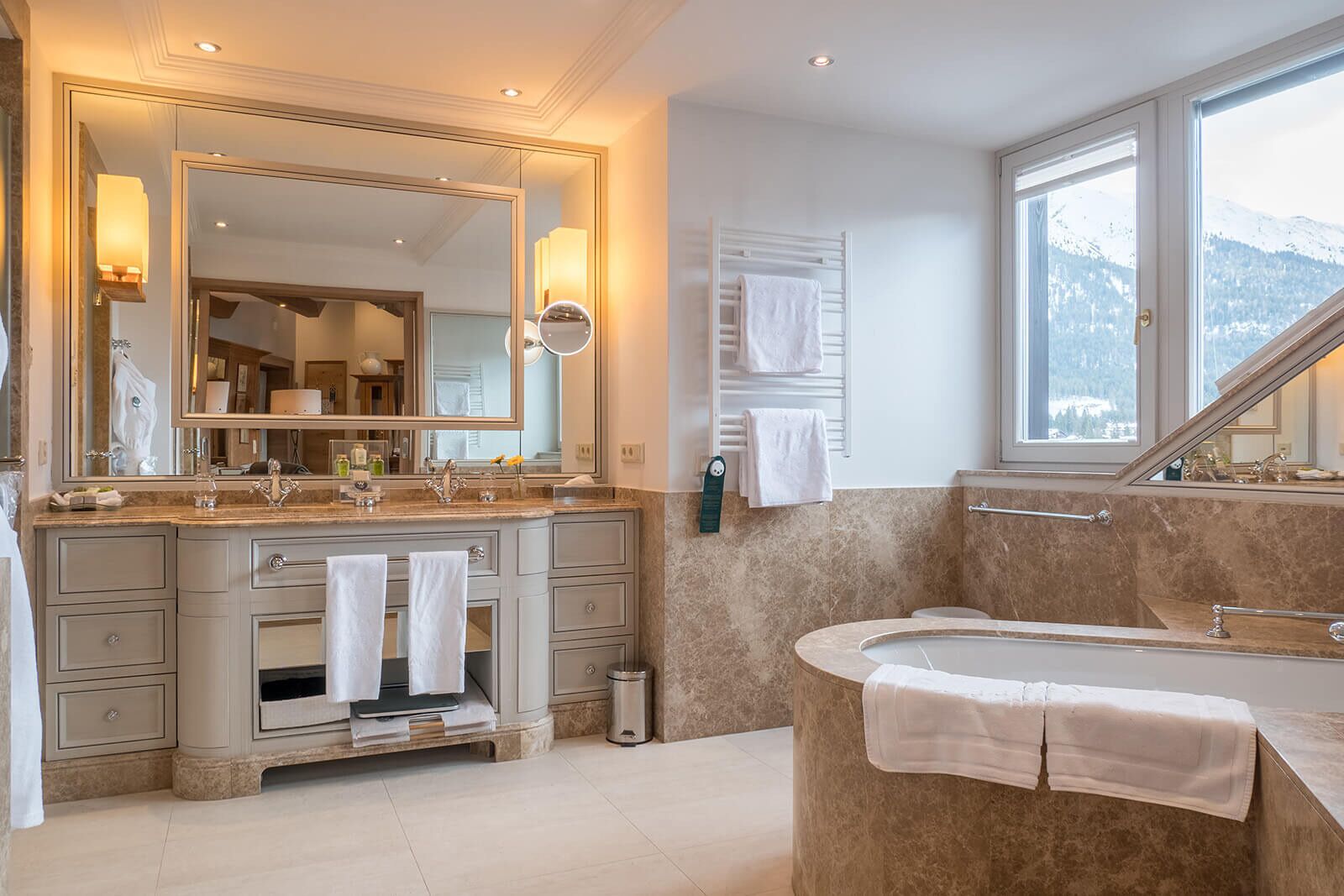 A modern bathroom with a large mirror, a bathtub, and a window with a mountain view.