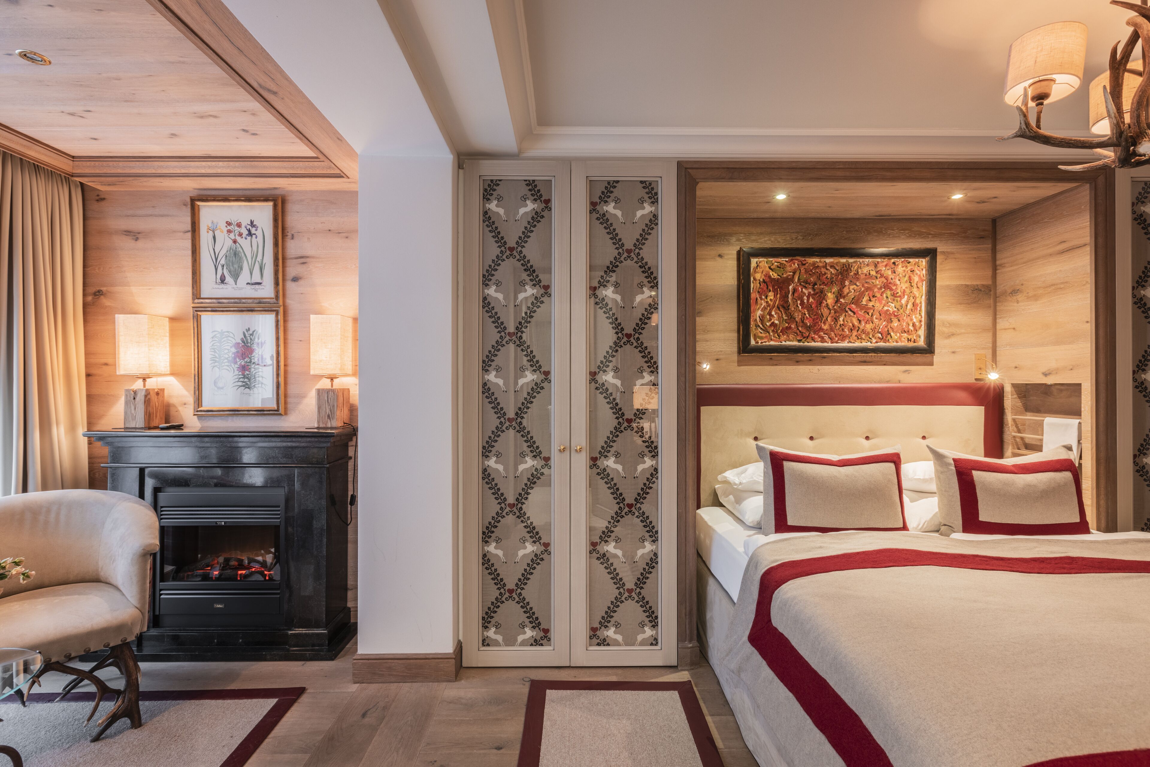 A bedroom with a fireplace, a bed with red bedding, and a large painting on the wall.