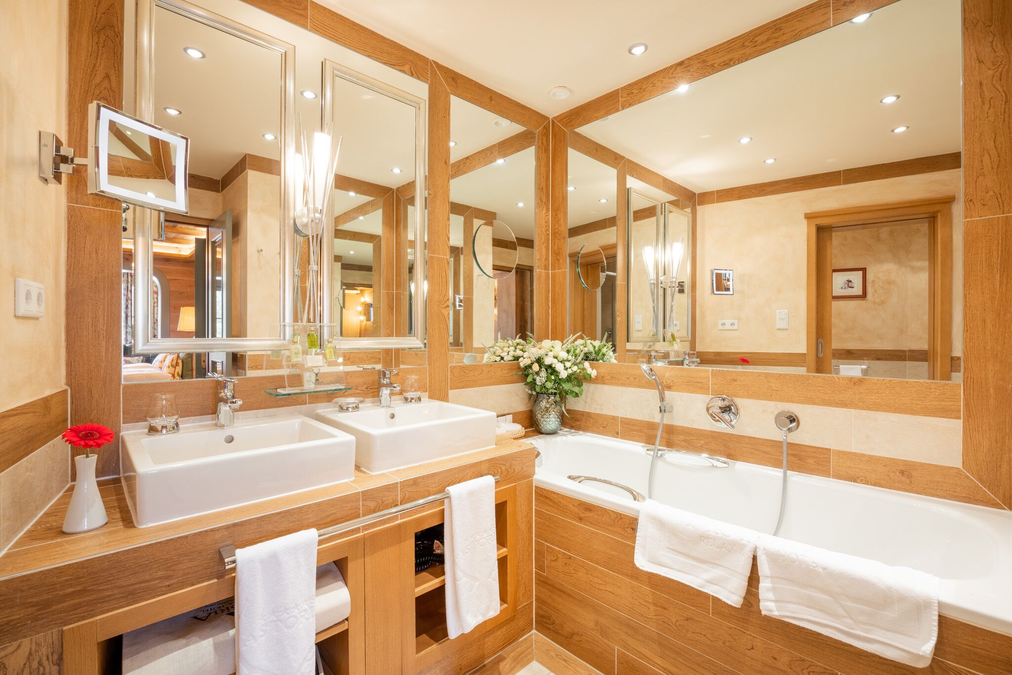 A modern bathroom with two sinks, a large mirror, and a bathtub.