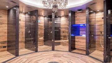 Um elevador moderno com projeto circular no chão, um lustre central e uma área iluminada em azul ao fundo.