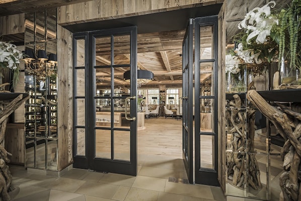 A wooden interior with a large open door leading to a dining area.