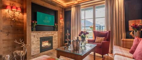 A cozy living room with a fireplace, a red armchair, a plaid sofa, and a glass coffee table.
