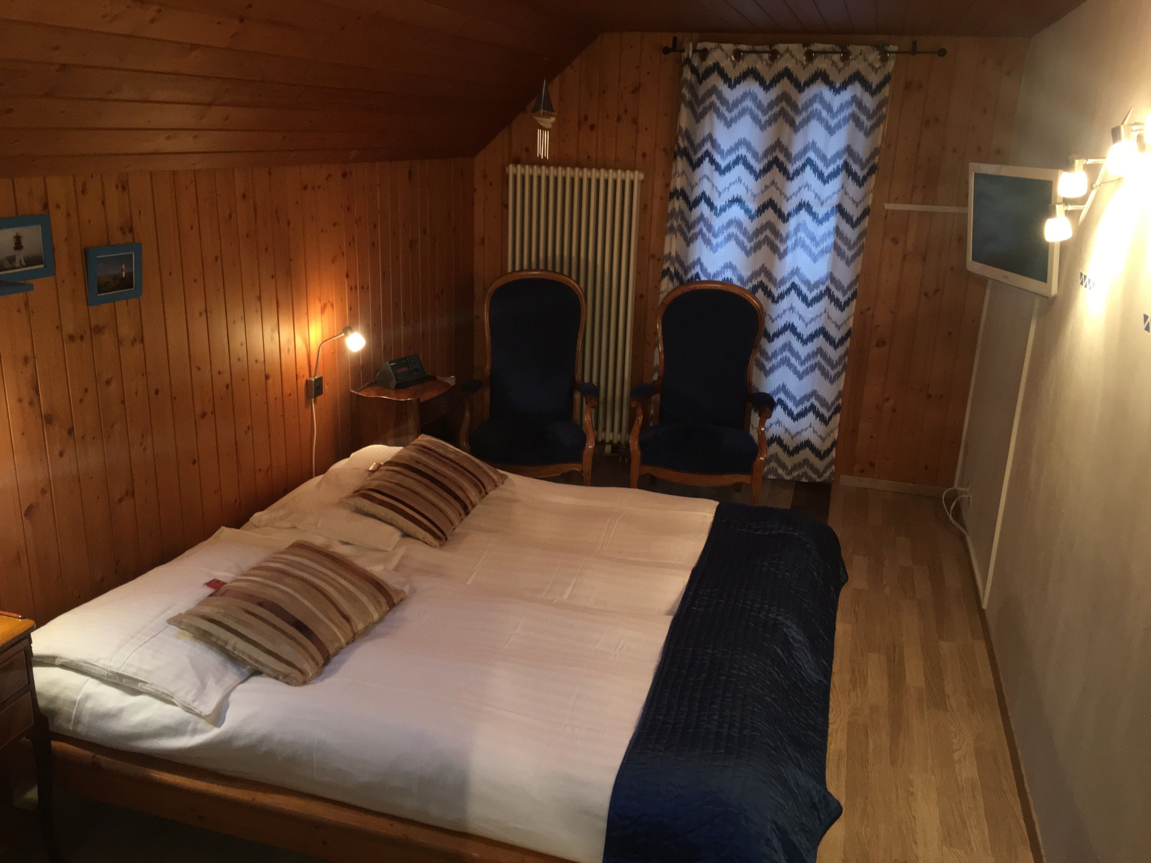Ein Zimmer mit Holzwänden, einem Bett, zwei Sesseln, einem kleinen Tisch mit Lampe und einem Fernseher.